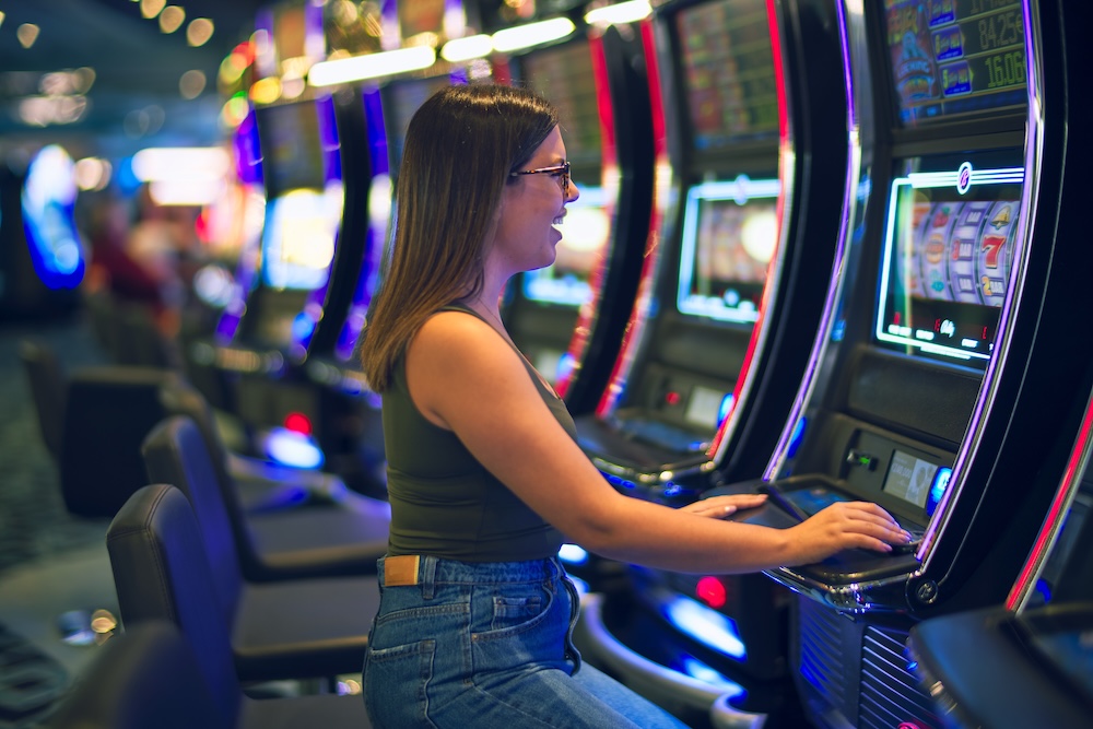 Young beautiful woman smiling happy and confident. Sitting with smile on face playing slot machine at casino
