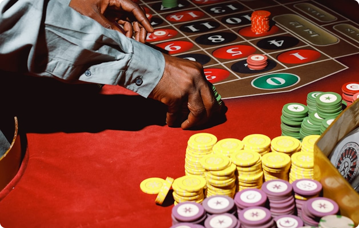 A person placing chips on a roulette table surrounded by stacks of colorful casino chips.