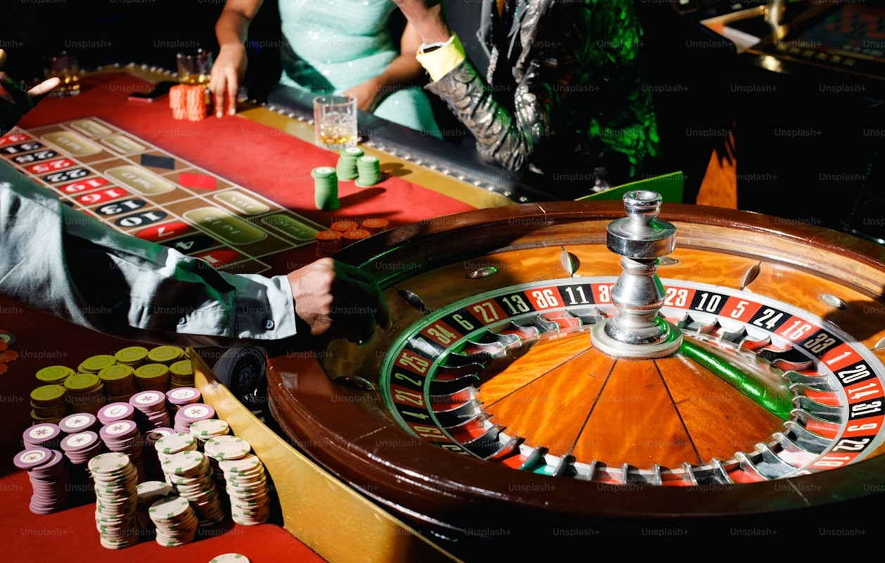A roulette wheel spinning beside players placing bets and stacks of colorful chips on the table.
