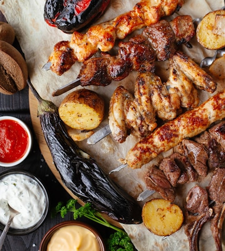 Mixed grilled skewers with chicken, beef, vegetables, roasted potatoes, and dipping sauces on a platter.