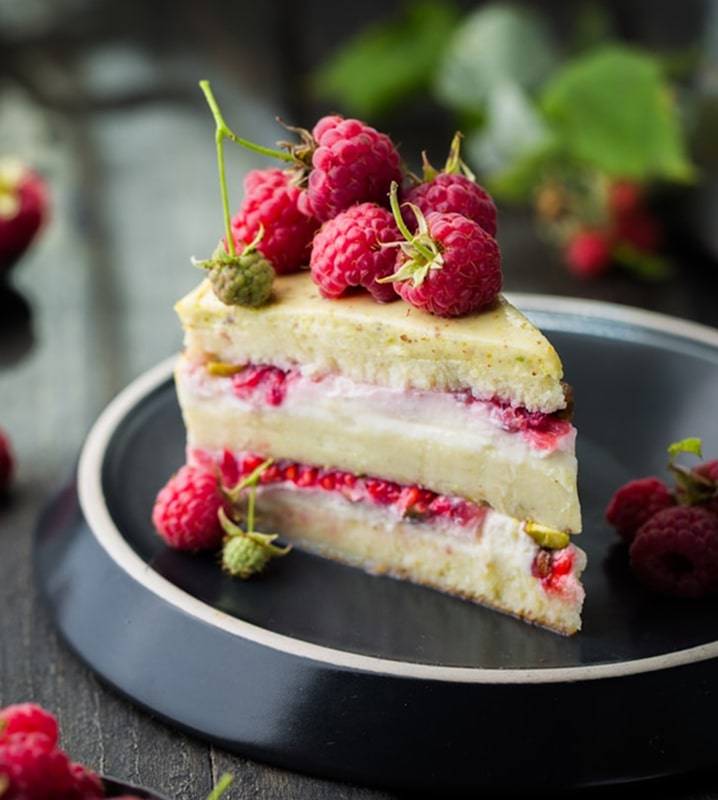 Slice of raspberry cream cake topped with fresh raspberries.